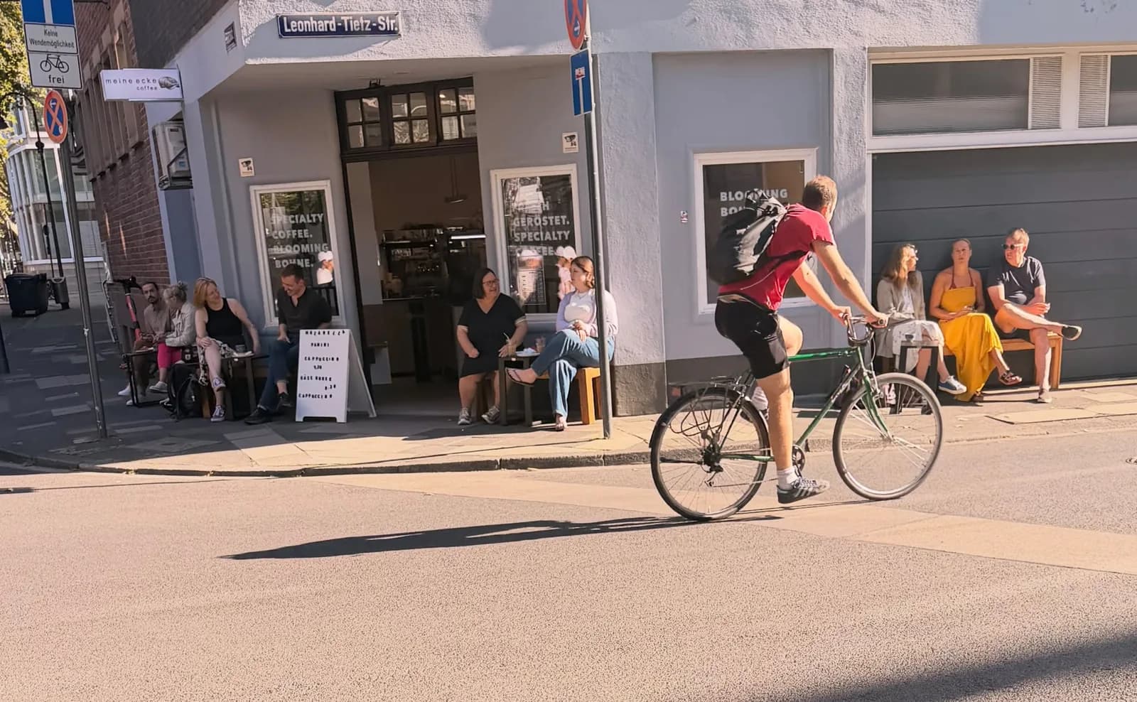 Radfahrer passiert das Eckcafé mit Gästen auf den Bänken