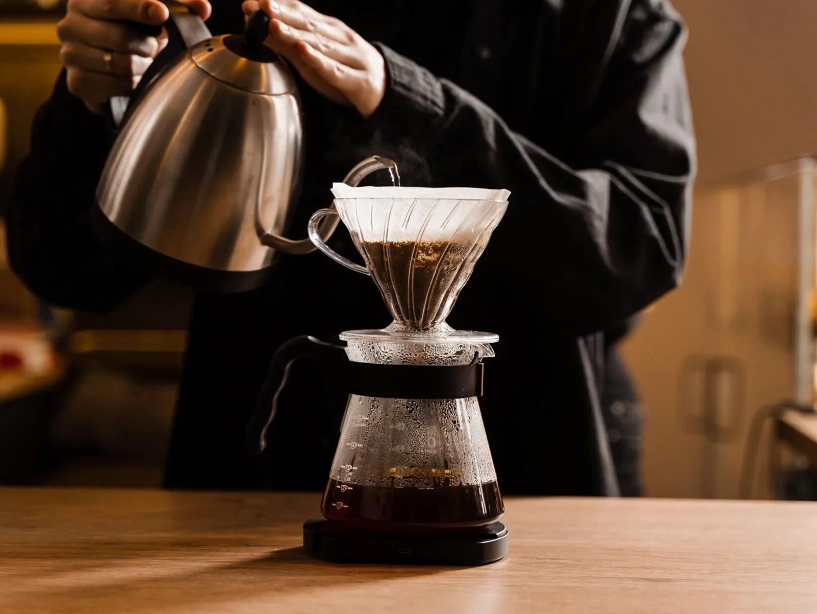 Barista gießt mit dem Schwanenhalskessel Wasser in den V60-Filter
